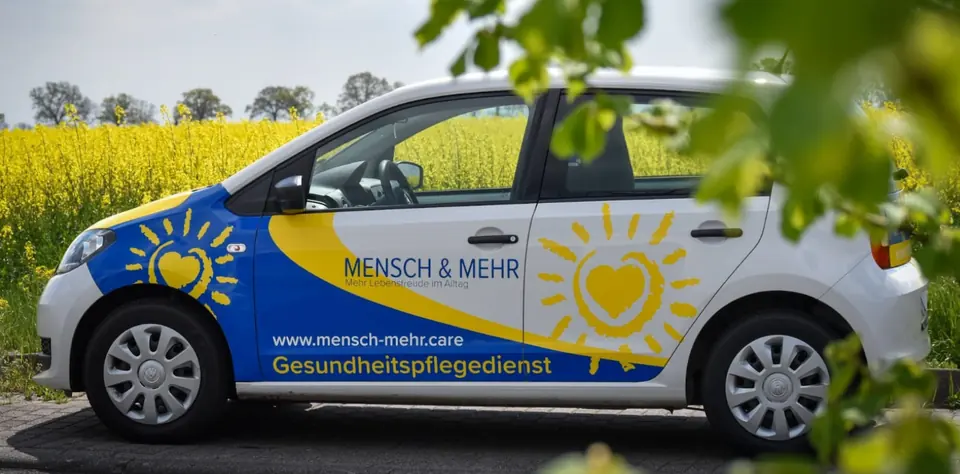 Firmenwagen von MENSCH & MEHR vor einem blühenden Rapsfeld