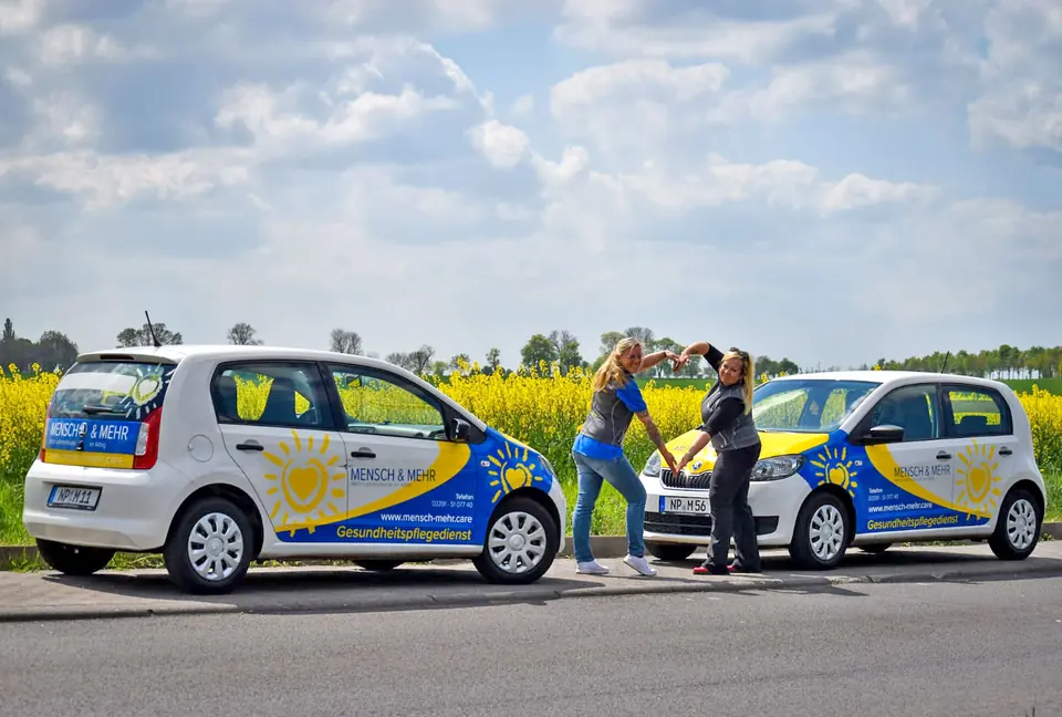 Zwei Kolleginnen formen zwischen den Firmenwagen ein Herz