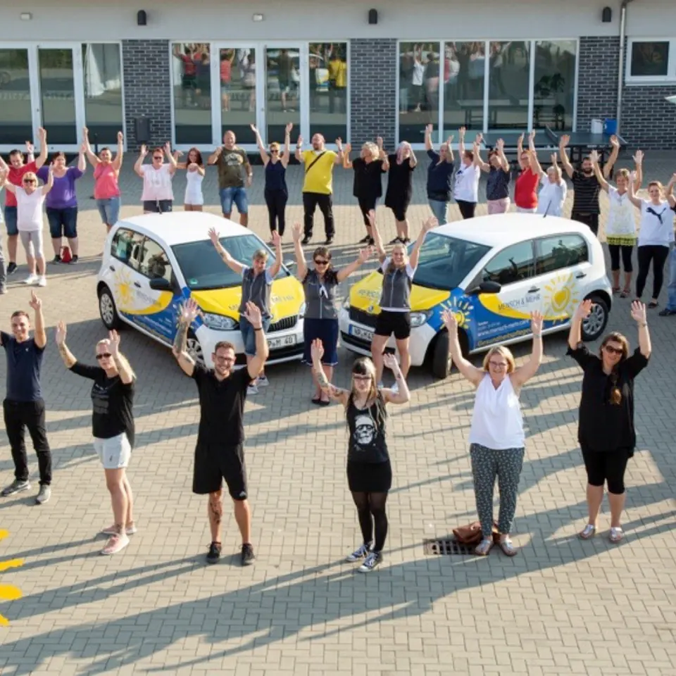 Das Team von MENSCH & MEHR springt vor zwei Firmenwagen in die Luft